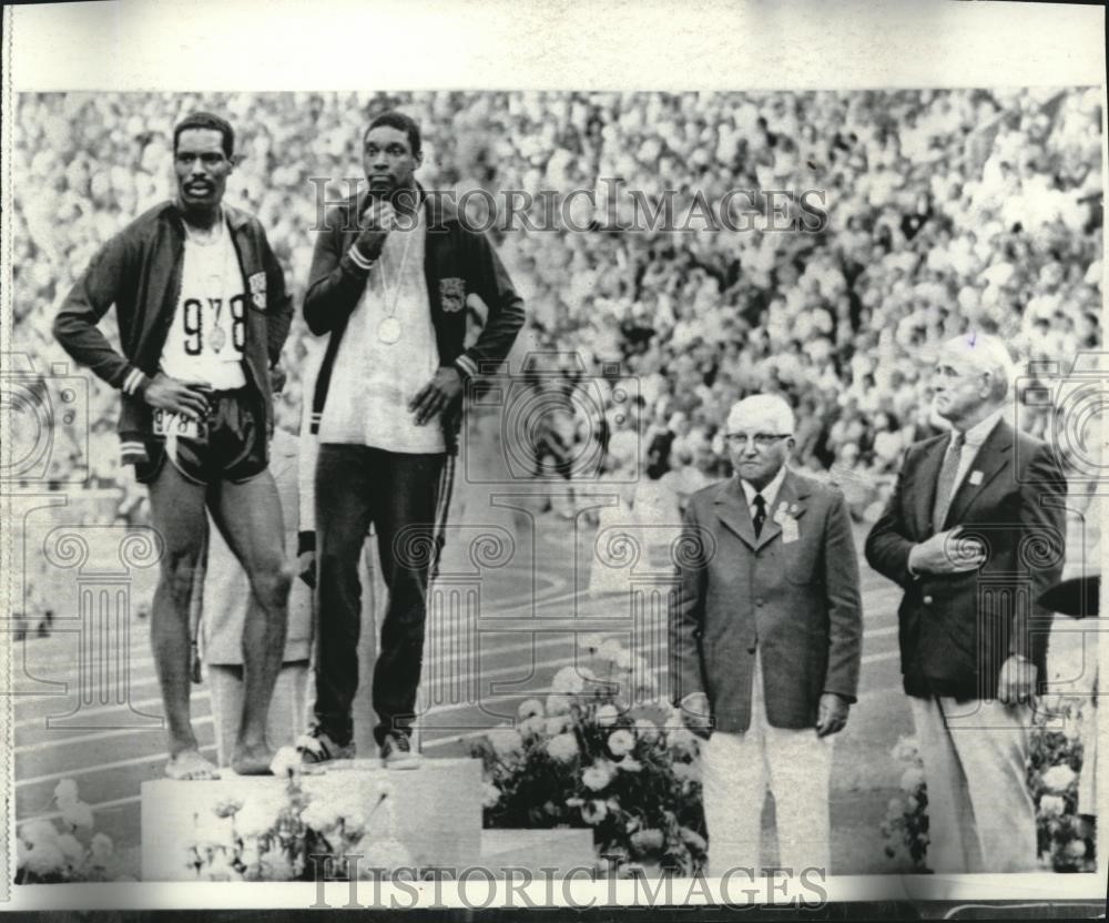 L’attitude dubitative de Wayne Collett (à gauche) et de Vince Matthews (au centre) contraste avec celle que prescrit habituellement le protocole : corps bien droit, yeux fixés sur le drapeau. Source : Associated Press via Wikimedia